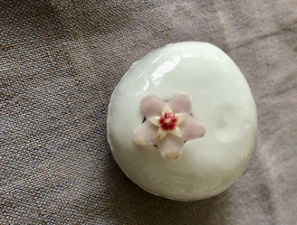 A delicate ceramic piece with smooth curves and a matte finish displayed on a wooden pedestal.