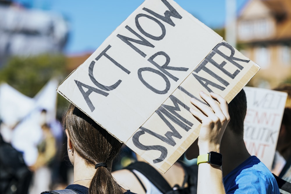a woman holding a sign that says act now or summer
