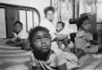 An African American woman and several children sitting on a bed in an apartment.