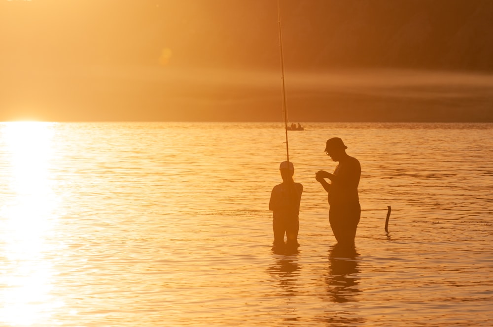 a father and son fishing in the lake at sunset