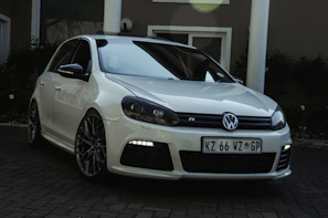 A light gray Volkswagen hatchback parked near a modern building.