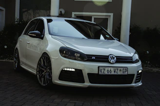 A light gray Volkswagen hatchback parked near a modern building.