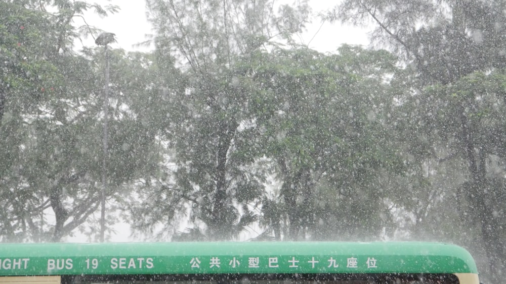 a green and white bus driving down a rain soaked street