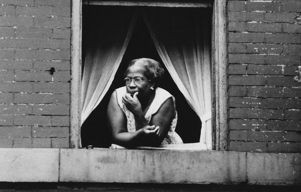 A woman leaning against an open windowsill, looking out.