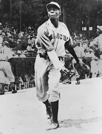 A baseball player in mid-action about to throw a pitch. The athlete is wearing a uniform with 'March' written on the jersey, and a cap. In the background, a crowd is visible, likely in a stadium setting.