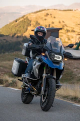 A rugged biker luggage bag strapped tightly to the back of a touring motorcycle on a winding road.