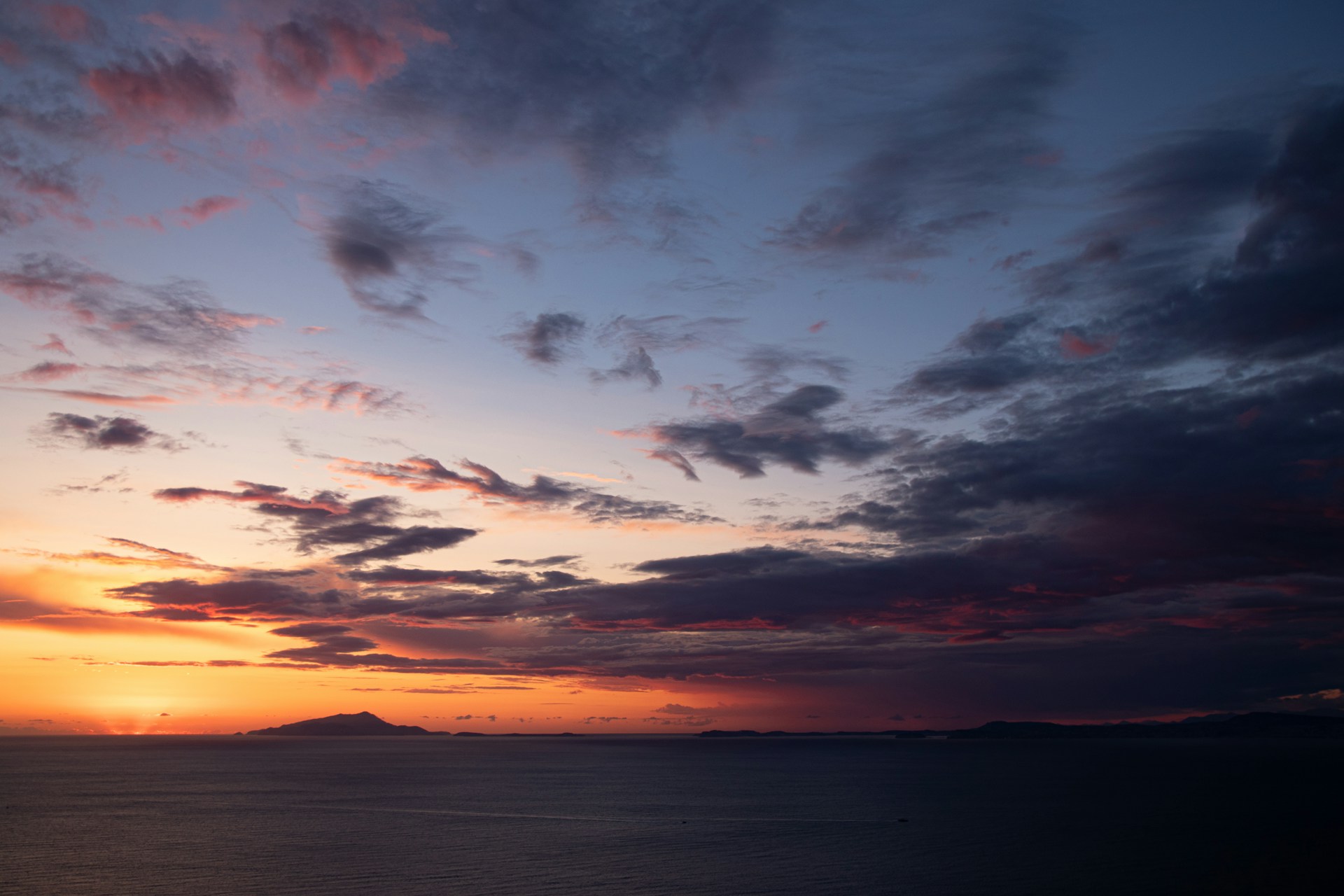 a sunset over a body of water with a mountain in the distance