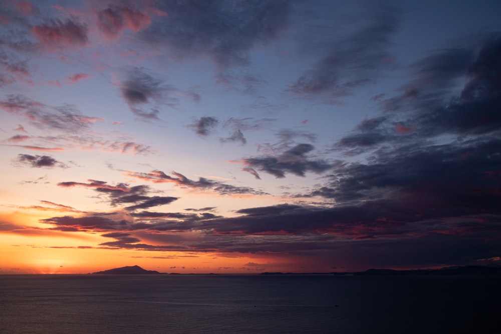 a sunset over a body of water with a mountain in the distance