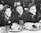 A group of children, smiling and seated at a table with empty bowls and cups, suggesting a school or communal meal setting. The focus is on three boys in the foreground, who appear to be enjoying each other's company.