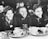 A group of children, smiling and seated at a table with empty bowls and cups, suggesting a school or communal meal setting. The focus is on three boys in the foreground, who appear to be enjoying each other's company.