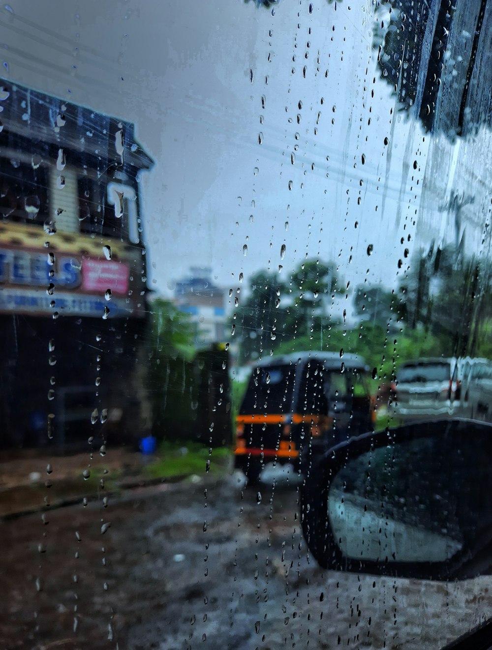 a rain soaked window with cars parked on the side of the road