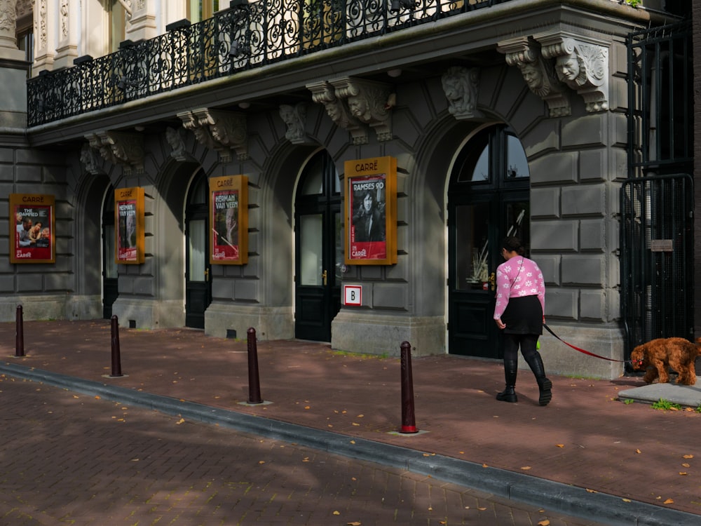 a woman walking a dog on a leash in front of a building