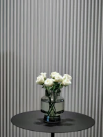 Minimalist arrangement of white lilies in a simple glass vase on a wooden table.