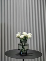 A delicate arrangement of preserved pink roses in a minimalist glass vase on a wooden table.