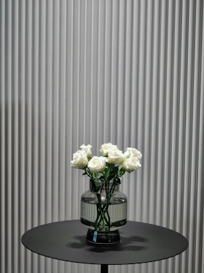 Minimalist arrangement of white roses and eucalyptus leaves in a simple glass vase on a wooden table.