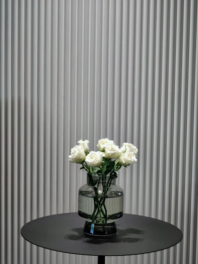 A minimalist luxury floral arrangement in a sleek black vase on a white table.