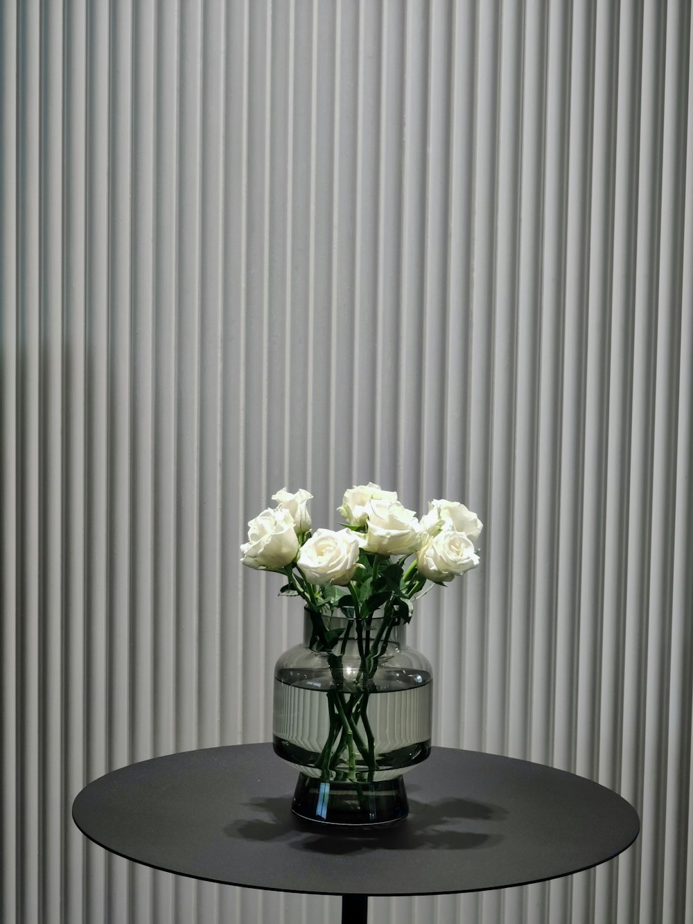 Eine Vase mit weißen Rosen auf einem schwarzen Tisch