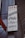 A vertical rectangular sign featuring text in both red and black colors. The sign promotes various food items including Lahmacun, Pide, Pizza, and Kahvalti. It is affixed to a building with a corrugated metal exterior and has an orange-red awning partially visible on the left side.