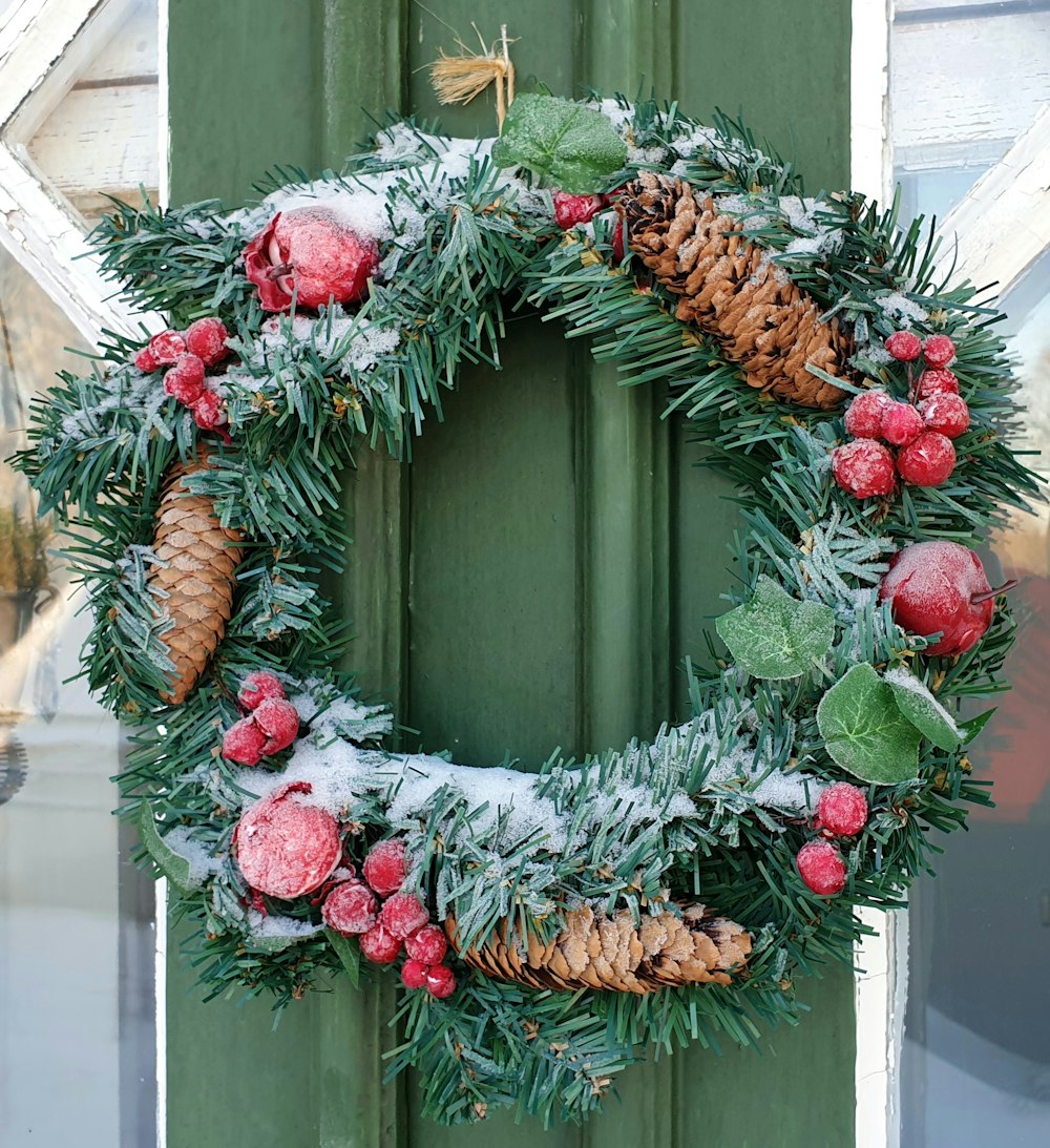 a green door with a wreath and pine cones on it