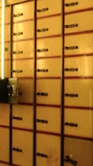Rows of vintage safety deposit boxes with an aged finish, each fitted with a metal latch and surrounded by a faintly illuminated space.