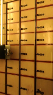 Rows of vintage safety deposit boxes with an aged finish, each fitted with a metal latch and surrounded by a faintly illuminated space.