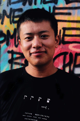 A young man wearing a bold graphic streetwear t-shirt standing against a colorful urban graffiti wall.