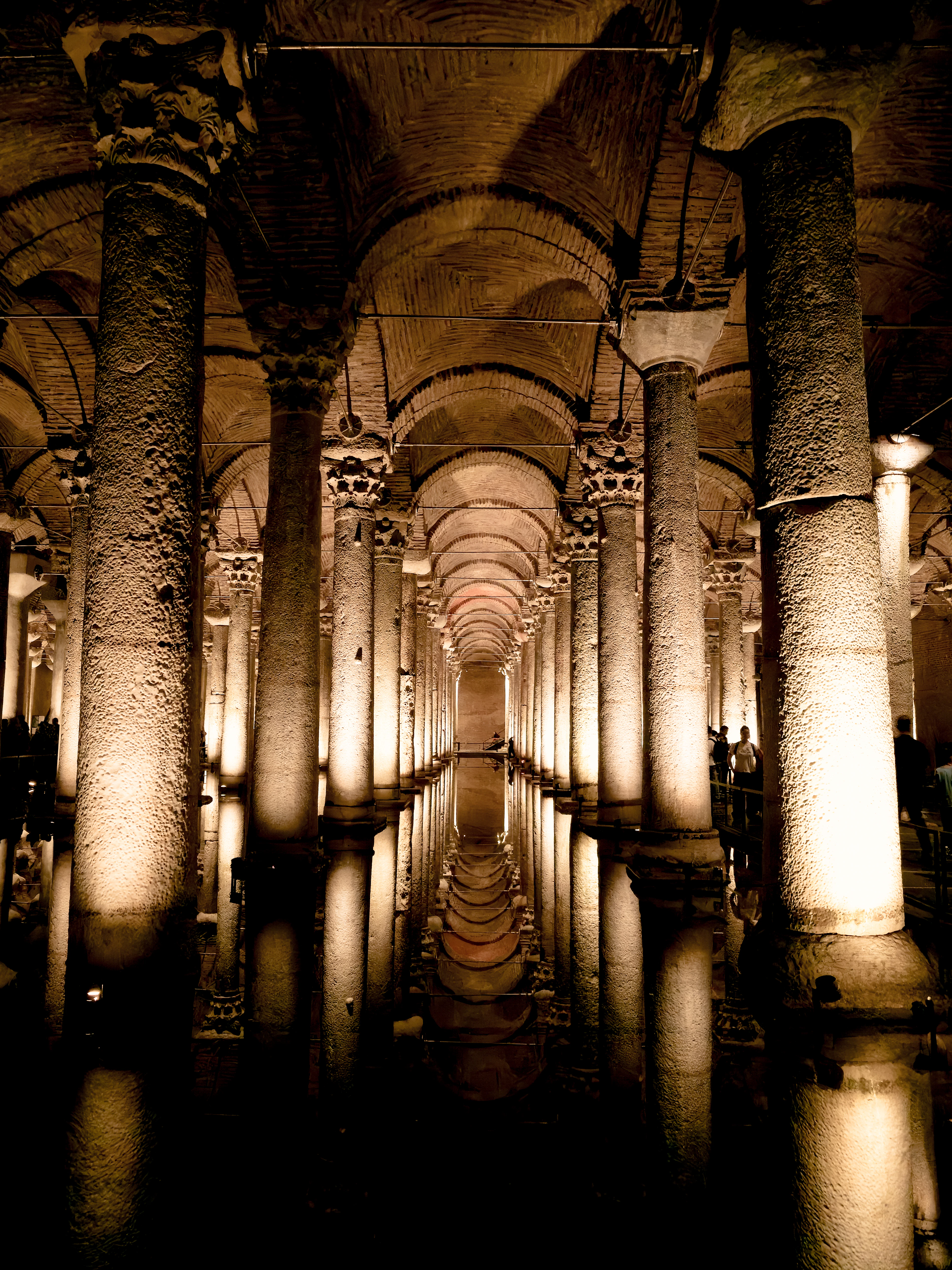 The colonnaded hall of the Basilica Cistern in Istanbul, rows of uplit marble columns and brick vaults receding into the dark and mirrored perfectly in the shallow water below