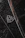 A close-up of a luxury car emblem adorned with raindrops, showcasing sleek chrome details against a dark, glossy surface.