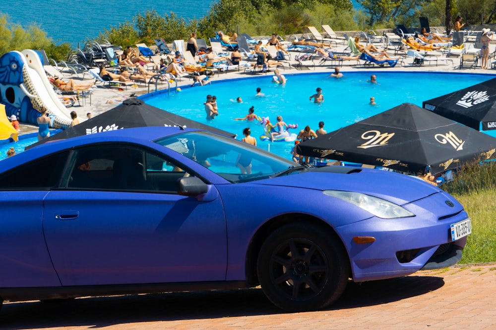 a blue sports car parked in front of a swimming pool