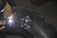 A welder is working on a large metal pipe, using a welding torch. The pipe is marked with white chalk symbols and numbers. The welder is wearing protective gloves and the bright welding light illuminates the immediate area.