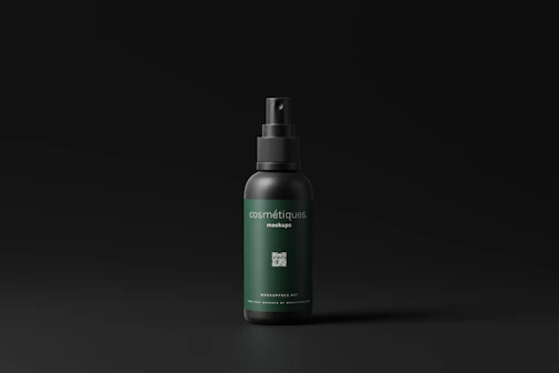 A cosmetic spray bottle with a dark green label and black cap is centered in a minimalistic setting. The label includes text and a small QR code. The background is a simple matte black, which highlights the product.