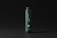 A dark green cylindrical bottle with a black cap stands against a dark background. The label on the bottle reads 'cosmétiques mockups' and includes a QR code as well as a website URL. The design is minimalistic and modern.