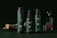 Three dark green cosmetic bottles with black caps are arranged in the foreground. Each bottle has the word 'cosmétiques' written on it. In the background, there is a glass decanter with a patterned design, partially filled with a brown liquid. A piece of wood is lying on the left side, adding a natural element.