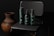 Three dark-colored cosmetic bottles are arranged on a dark, woven chair with an earthy-toned pottery vase next to it. The lighting is subdued, creating a sophisticated and sleek atmosphere.