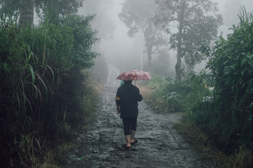 a woman walking down a dirt road holding an umbrella