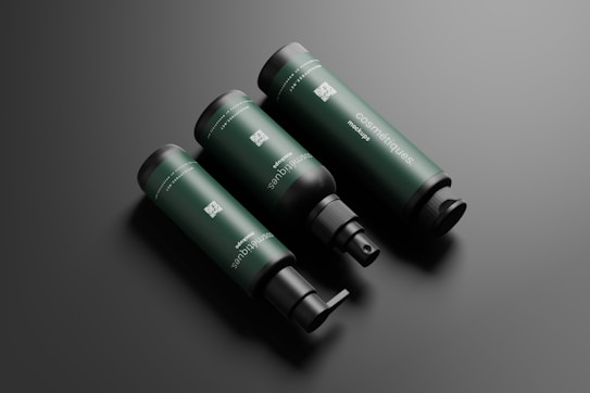 Three dark green cylindrical bottles with black caps and dispensers are arranged diagonally against a dark gray background. The bottles have 'cosm&eacute;tiques mockup' written on them in white text along with QR codes and other fine text details.