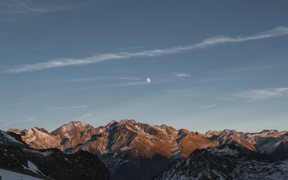 a view of a mountain range with a moon in the sky