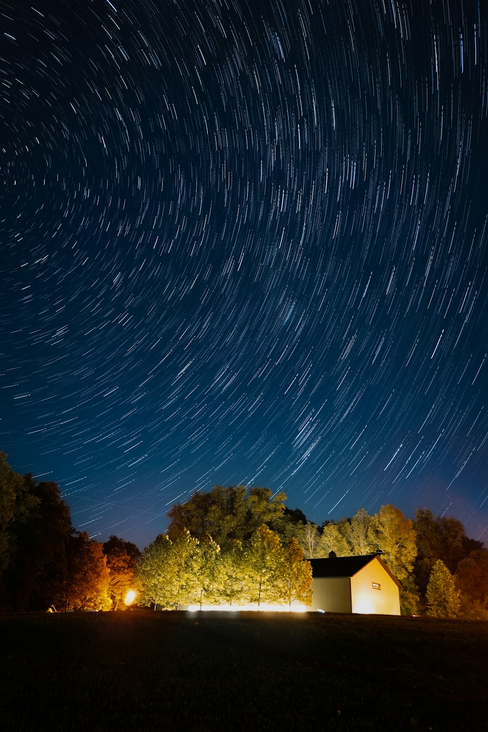 el cielo nocturno con una casa y árboles en primer plano