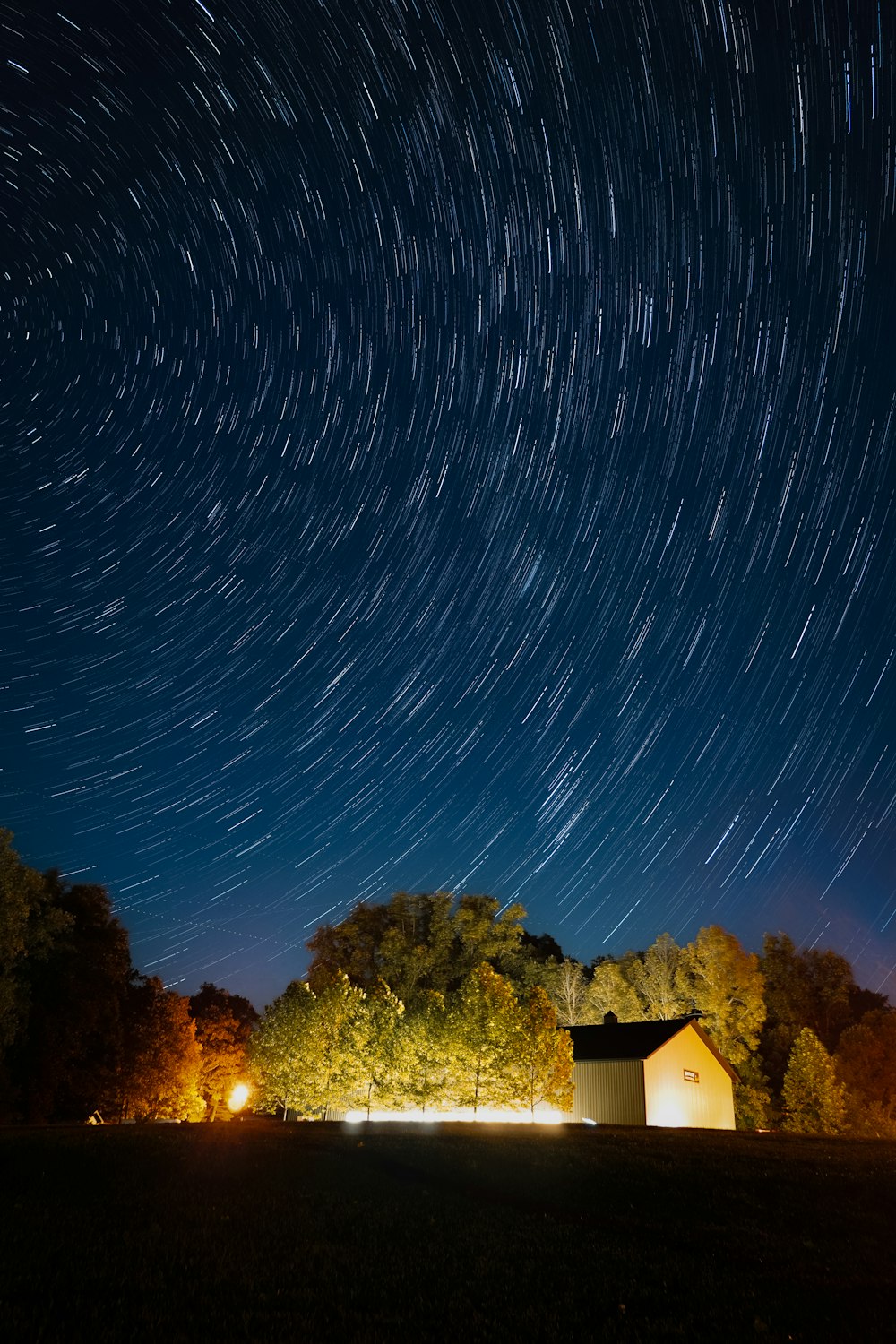 the night sky with a house and trees in the foreground