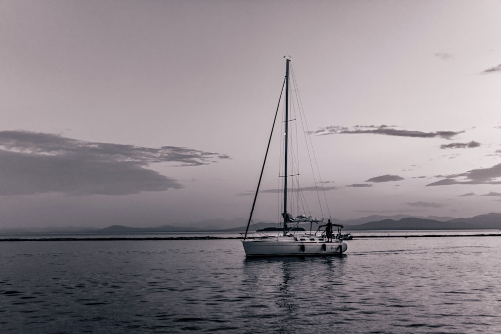 a sailboat floating on a body of water under a cloudy sky