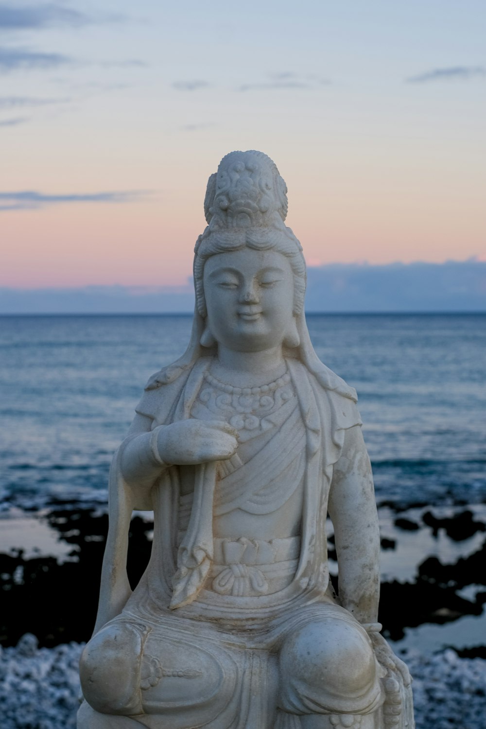 a white statue sitting on top of a beach next to the ocean
