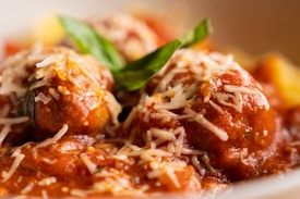 Meatballs covered in a rich tomato sauce topped with grated cheese are garnished with fresh basil. The dish appears appetizing and well-plated, with a focus on the textures of the cheese and sauce.
