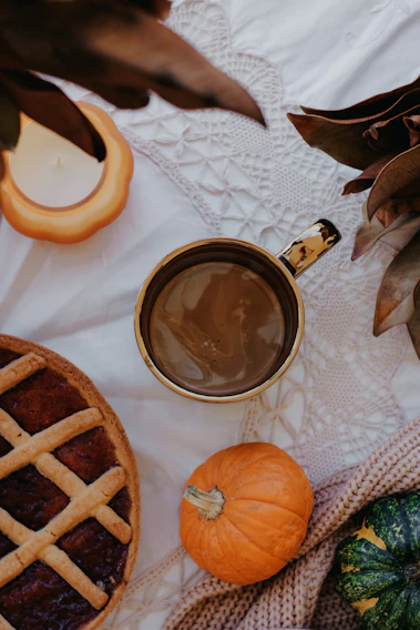 A warm, rustic kitchen table set with freshly baked pumpkin pies and autumn leaves scattered around.
