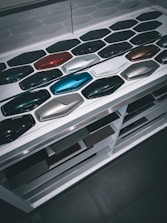 A display of various car paint color samples arranged in neat rows on a white surface. Each sample is shaped like a car body panel and showcases a different shade, ranging from dark greens and blues to reds, silvers, and blacks.