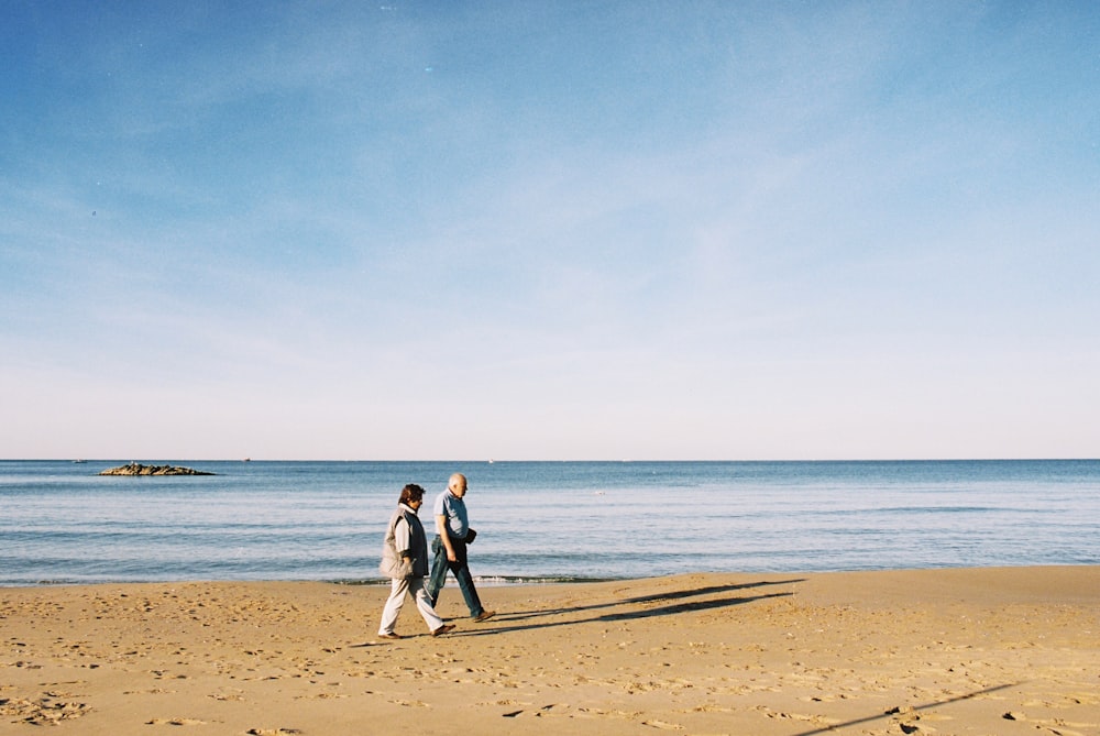 two people walking on a beach next to the ocean