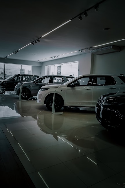 Several cars are displayed inside a modern, well-lit showroom with a sleek and polished floor. Large windows provide natural light.