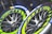 Two racing tires with vibrant yellow-green and blue accents are shown, featuring detailed tread patterns and the brand name Michelin visible on the sidewall. The rims are sleek and metallic with a modern design.