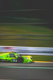 A bright green race car speeds along a track with motion blur, emphasizing its high velocity. The car has the number 34 printed on the side and is adorned with various sponsor logos.