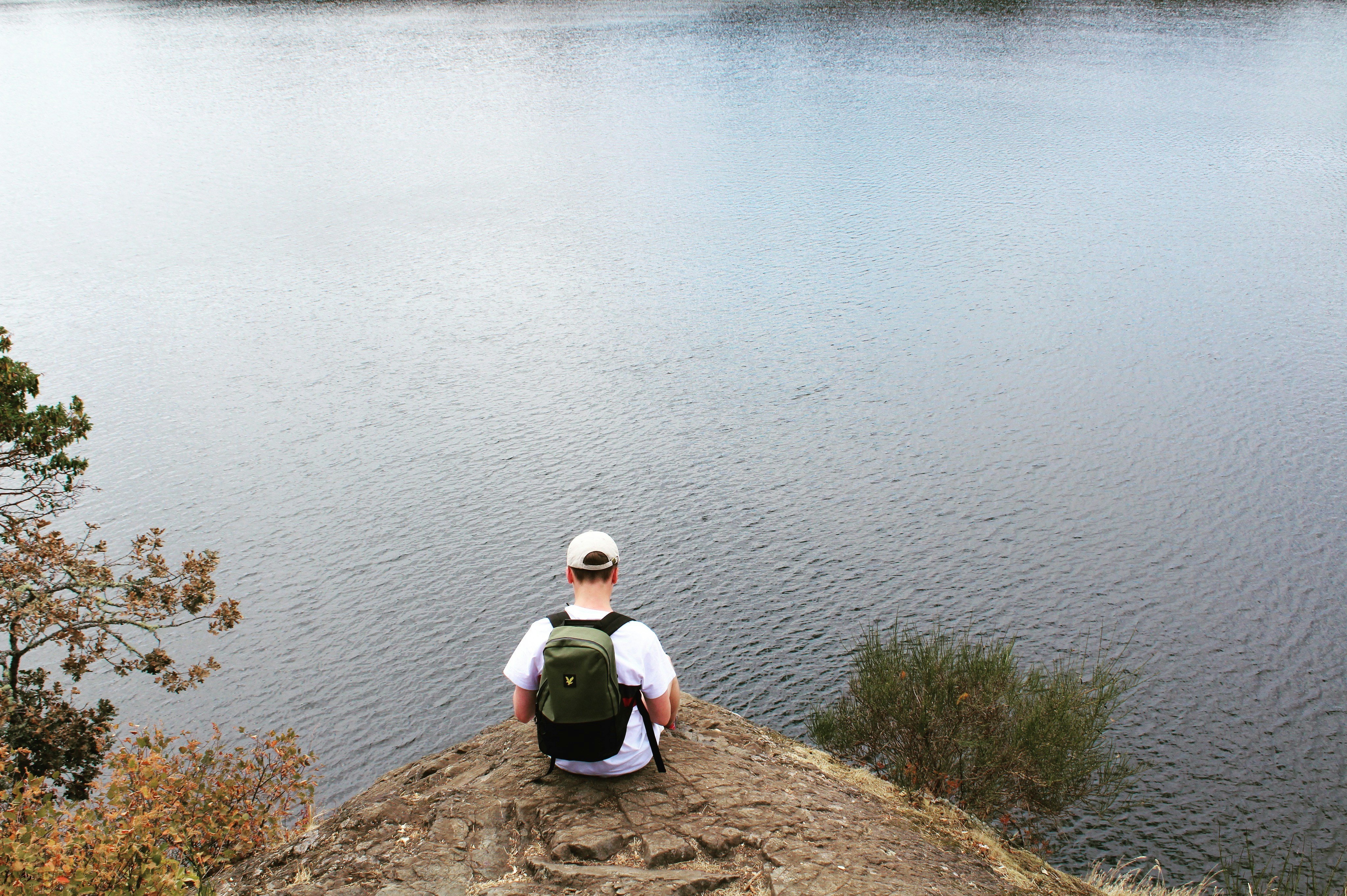a man sitting on top of a hill next to a lake