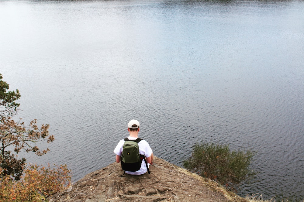 a man sitting on top of a hill next to a lake